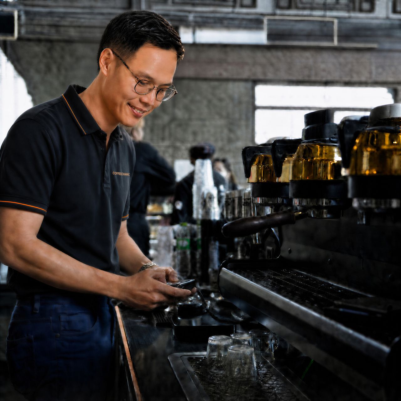 COFFEECHANIC technician in a branded polo shirt at work beside a commercial espresso machine.